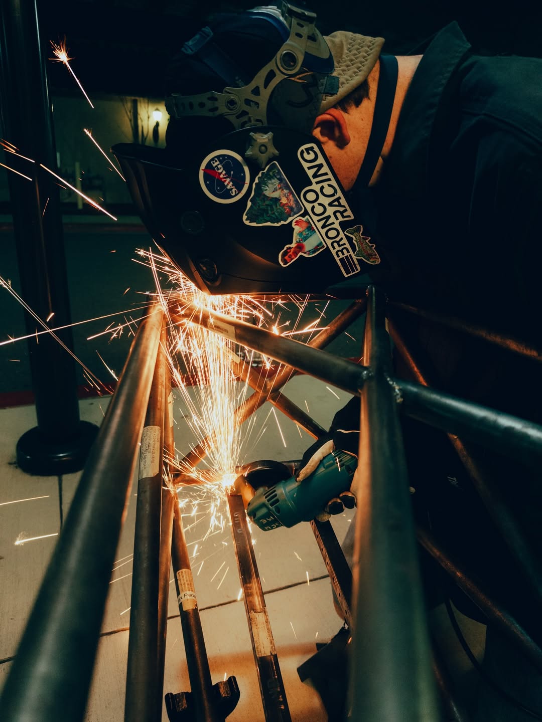 Team member angle grinding the Formula SAE chassis with sparks flying.